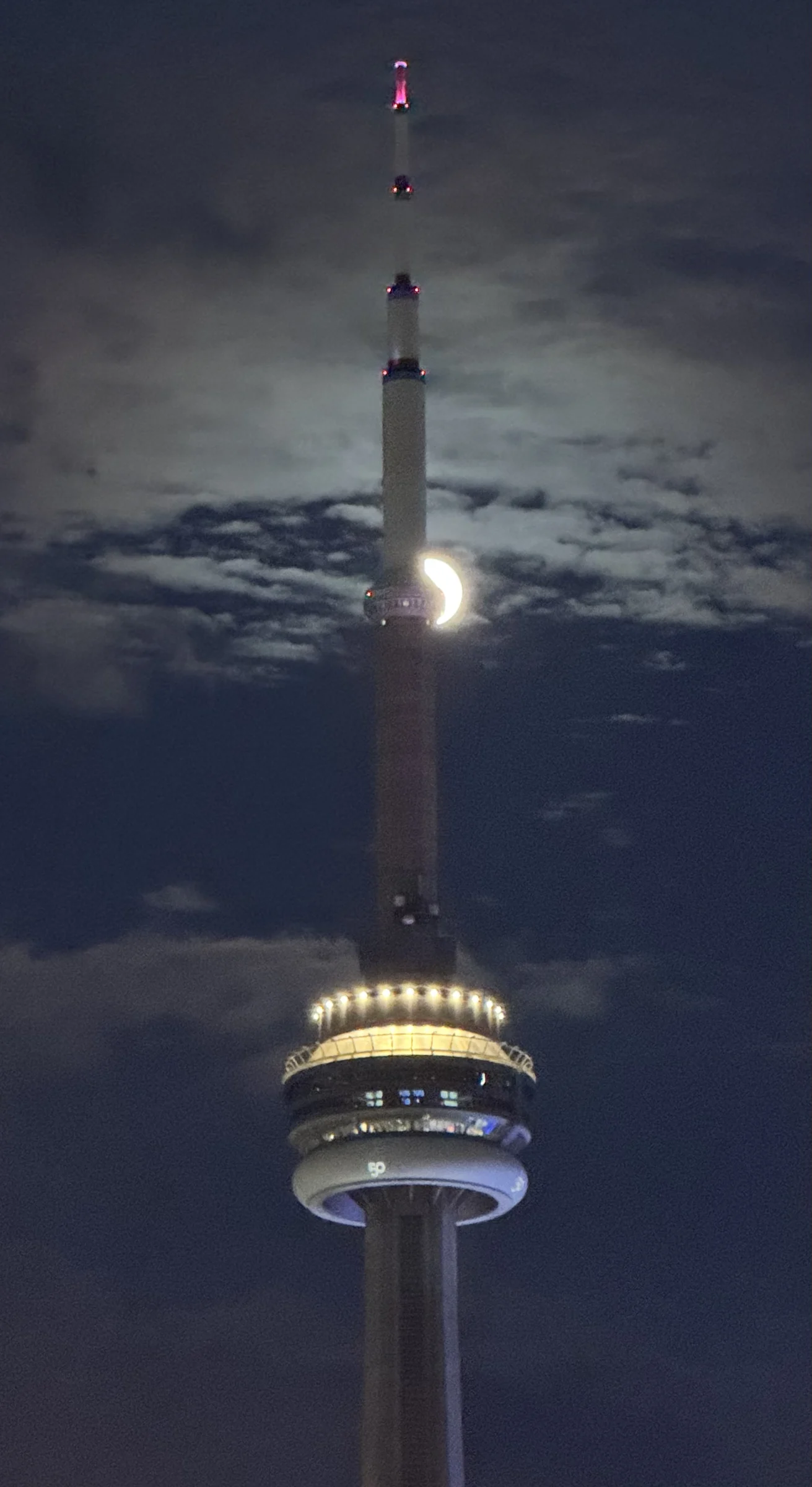 The CN Tower at night with a sliver of the moon emerging from behind it