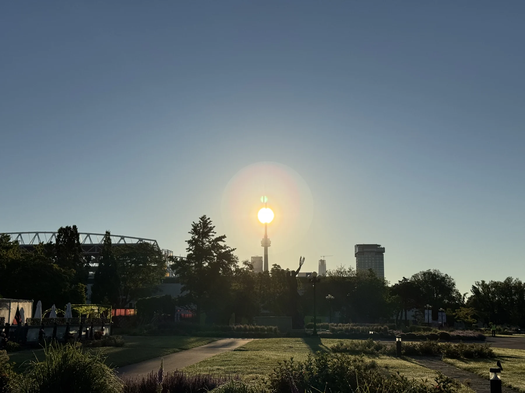 A wide view of a park at dawn with the sun on top of the distant CN Tower